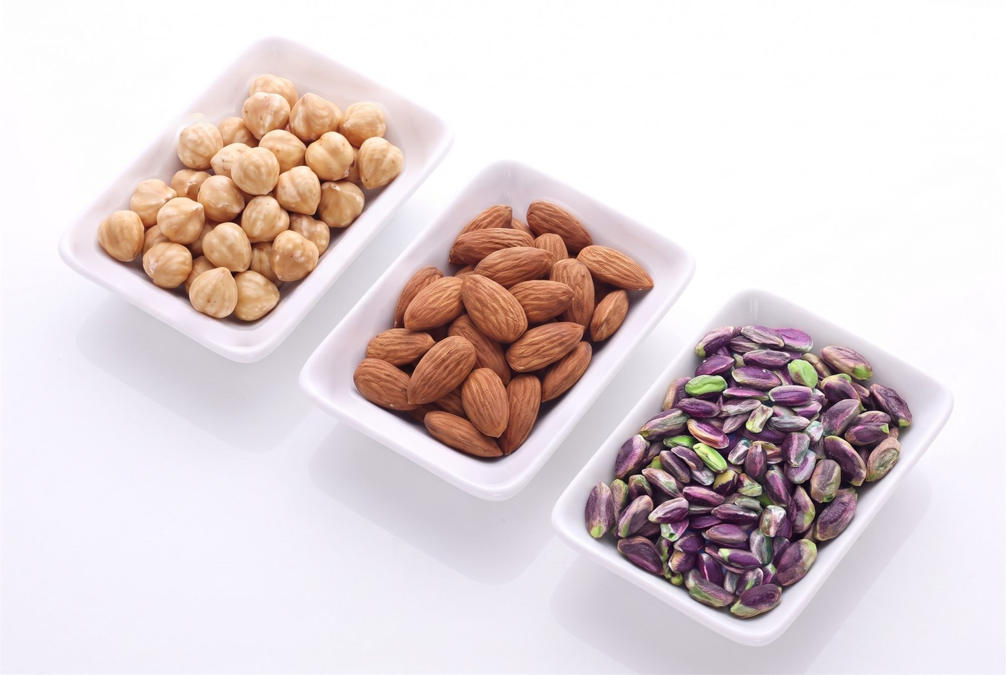 Three white trays with hazelnuts, almonds and Bronte pistachios